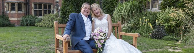 Bride and Groom sat on a bench outside the front of the college, smiling together.