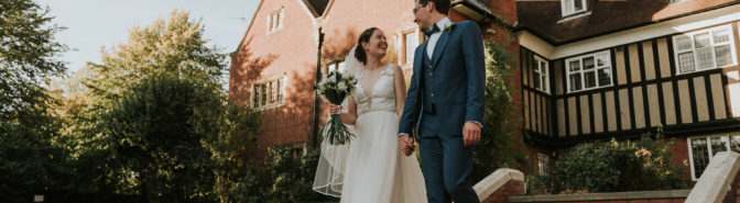 Bride and Groom walking down the steps outside the Woolf Institute smiling and looking at each other.